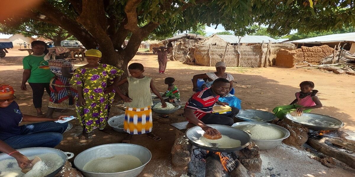 Women and youth roasting cassava into gari over open fires in a rural community